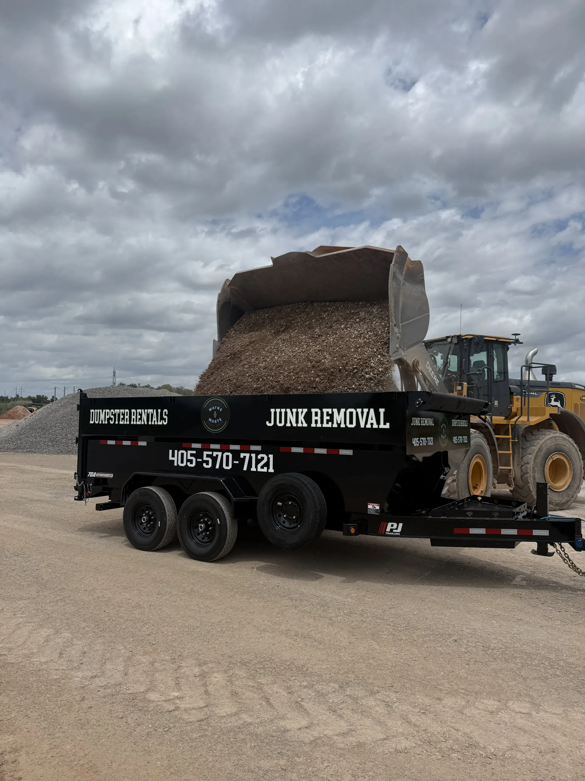 Dump truck hauling a large concrete block on a gravel lot under cloudy skies