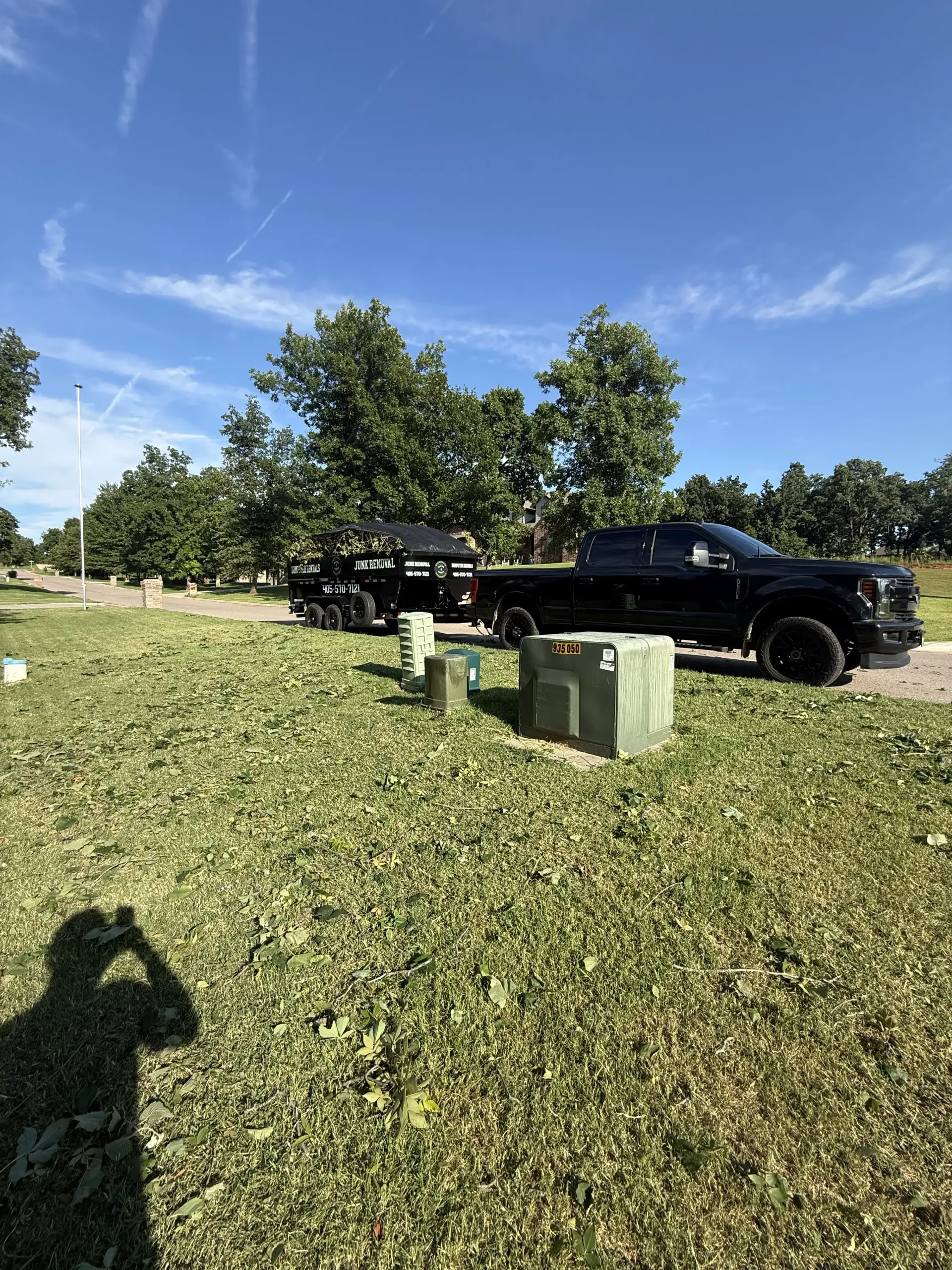 Black pickup trucks parked on a grassy roadside near utility boxes under a blue sky.
