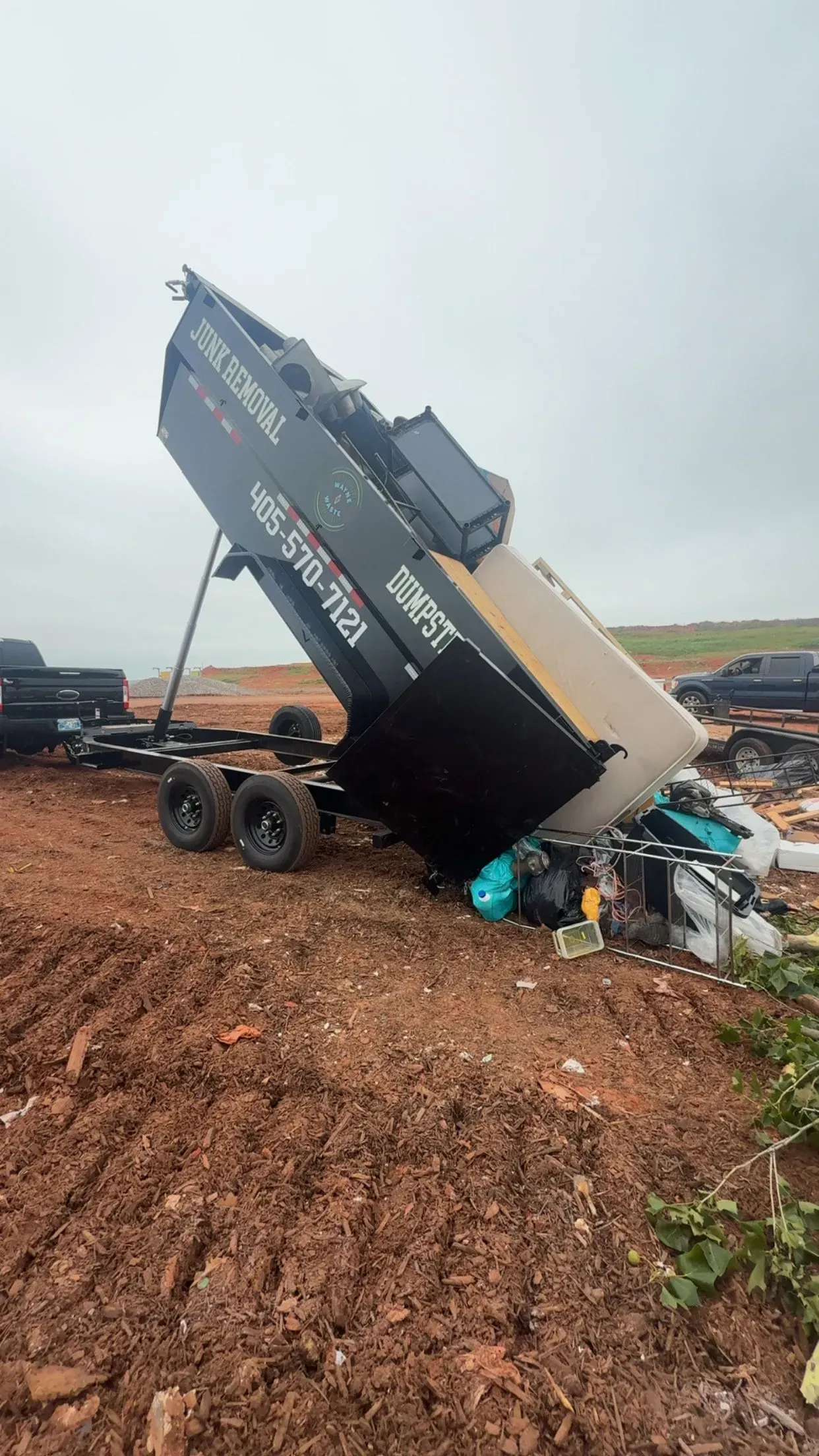 Overturned black truck on a muddy roadside, with debris scattered around and a cloudy sky.