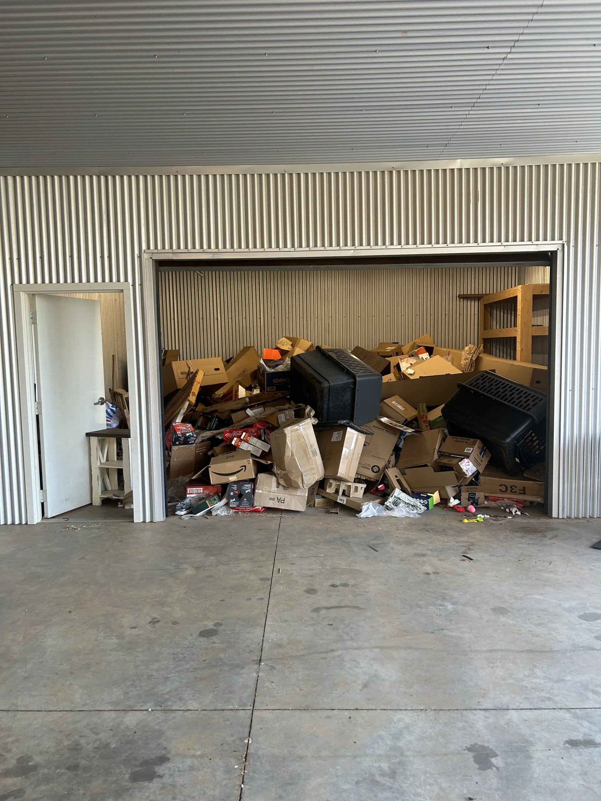 Overflowing storage unit with piles of clutter and debris spilling into the doorway.
