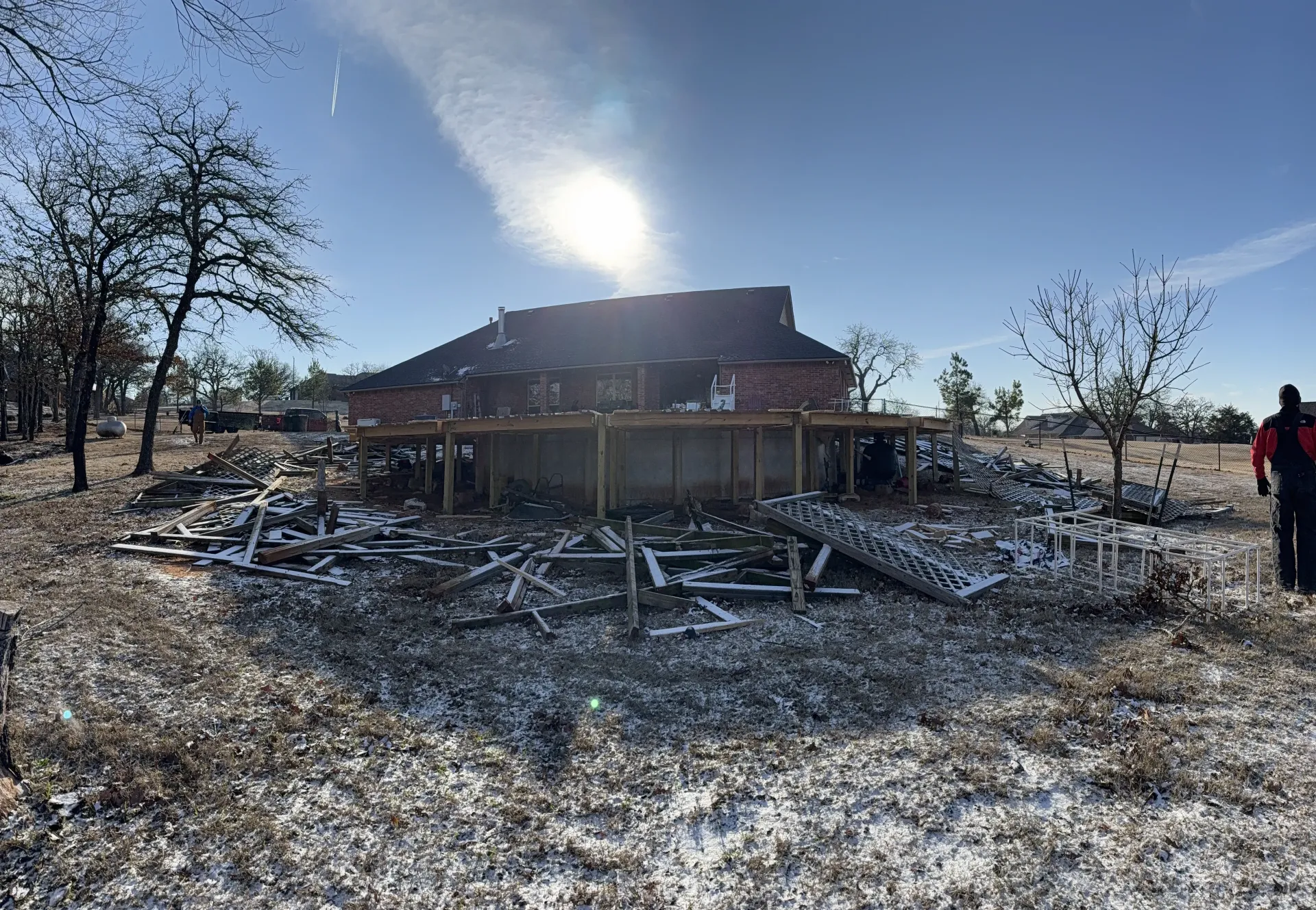 Collapsed house with snow-covered rubble and a person standing at the right edge under a bright winter sky