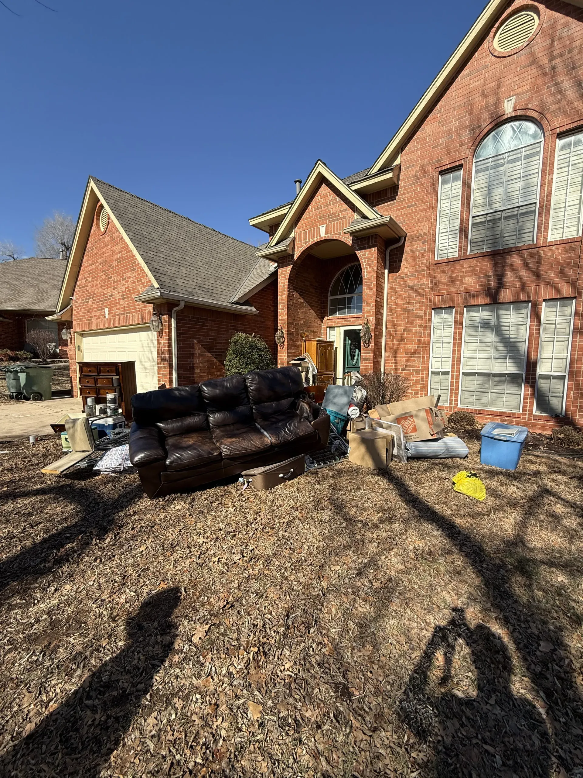 Brick house exterior with garage, covered porch, and stacked mulch bags in the driveway under clear blue sky