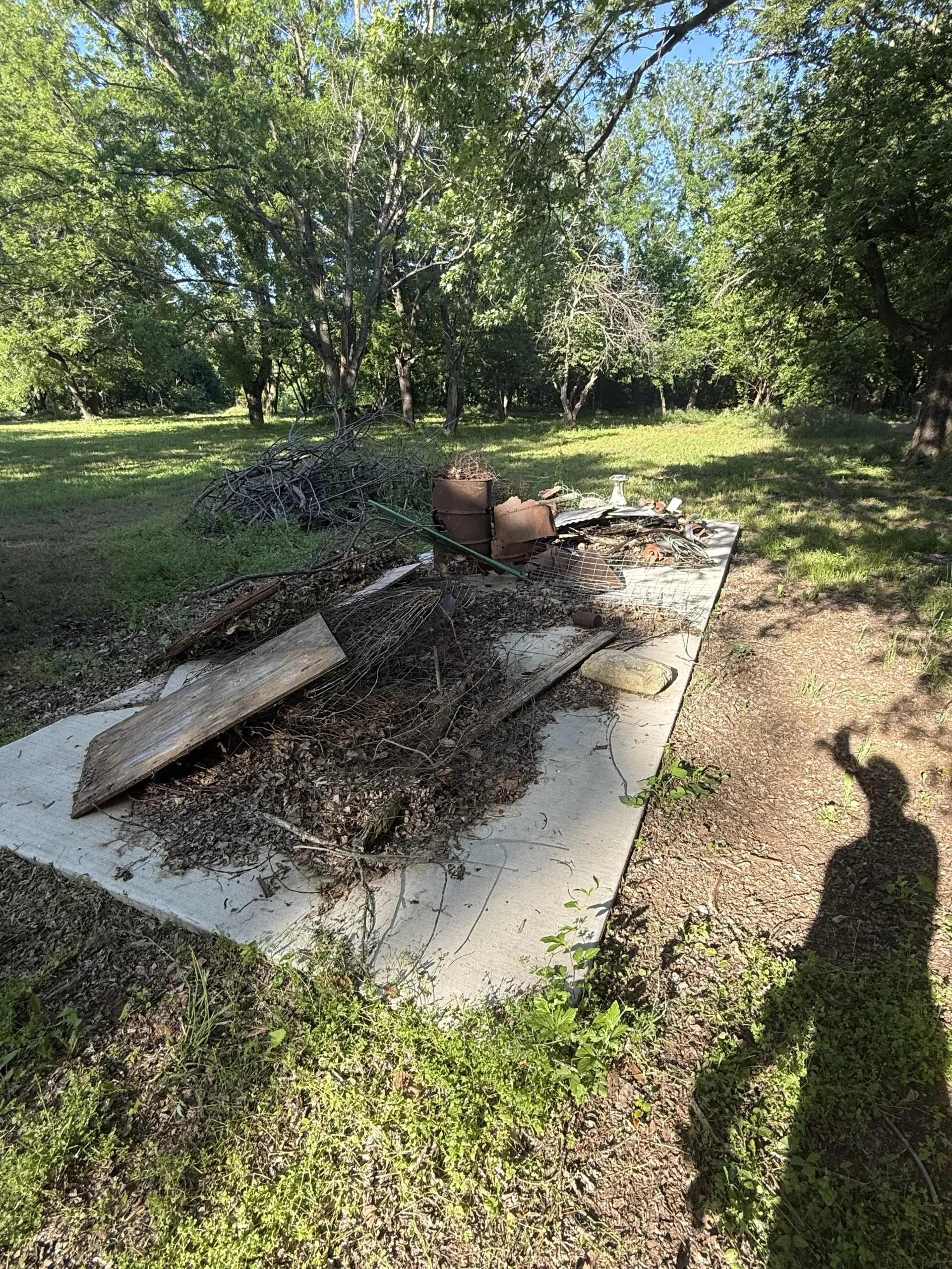 Backyard fire pit with charred debris on a concrete slab, surrounded by trees and grass.
