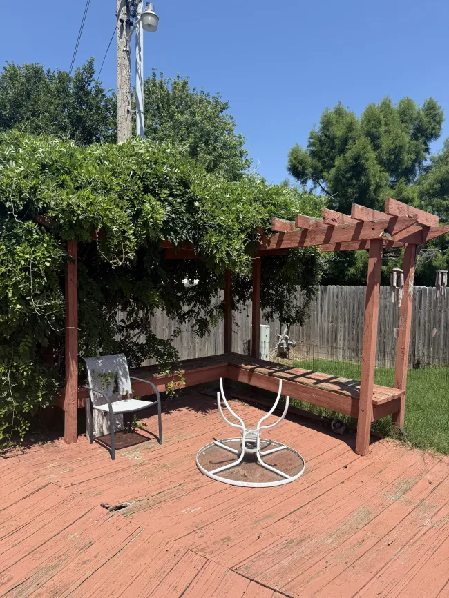 Backyard patio with red brick pavers, wooden pergola, vine-covered fence, and a metal patio table and chairs