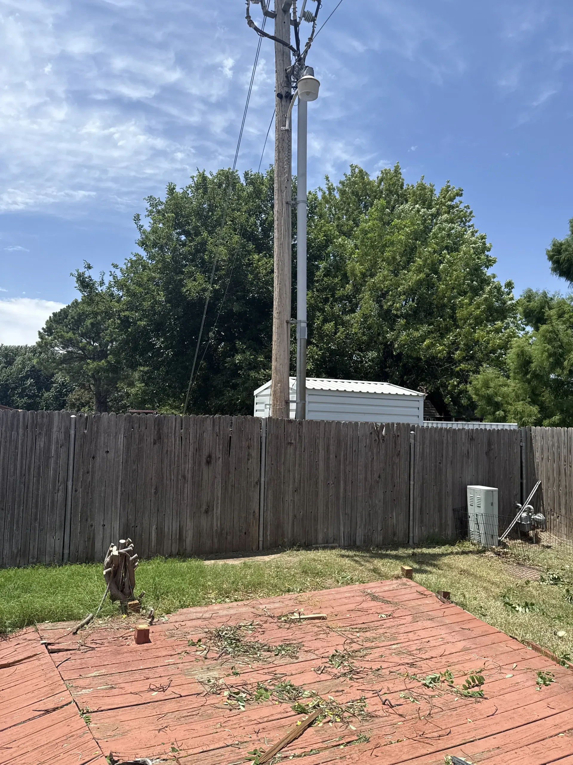 Backyard with wooden fence, utility pole, and trees under a partly cloudy sky