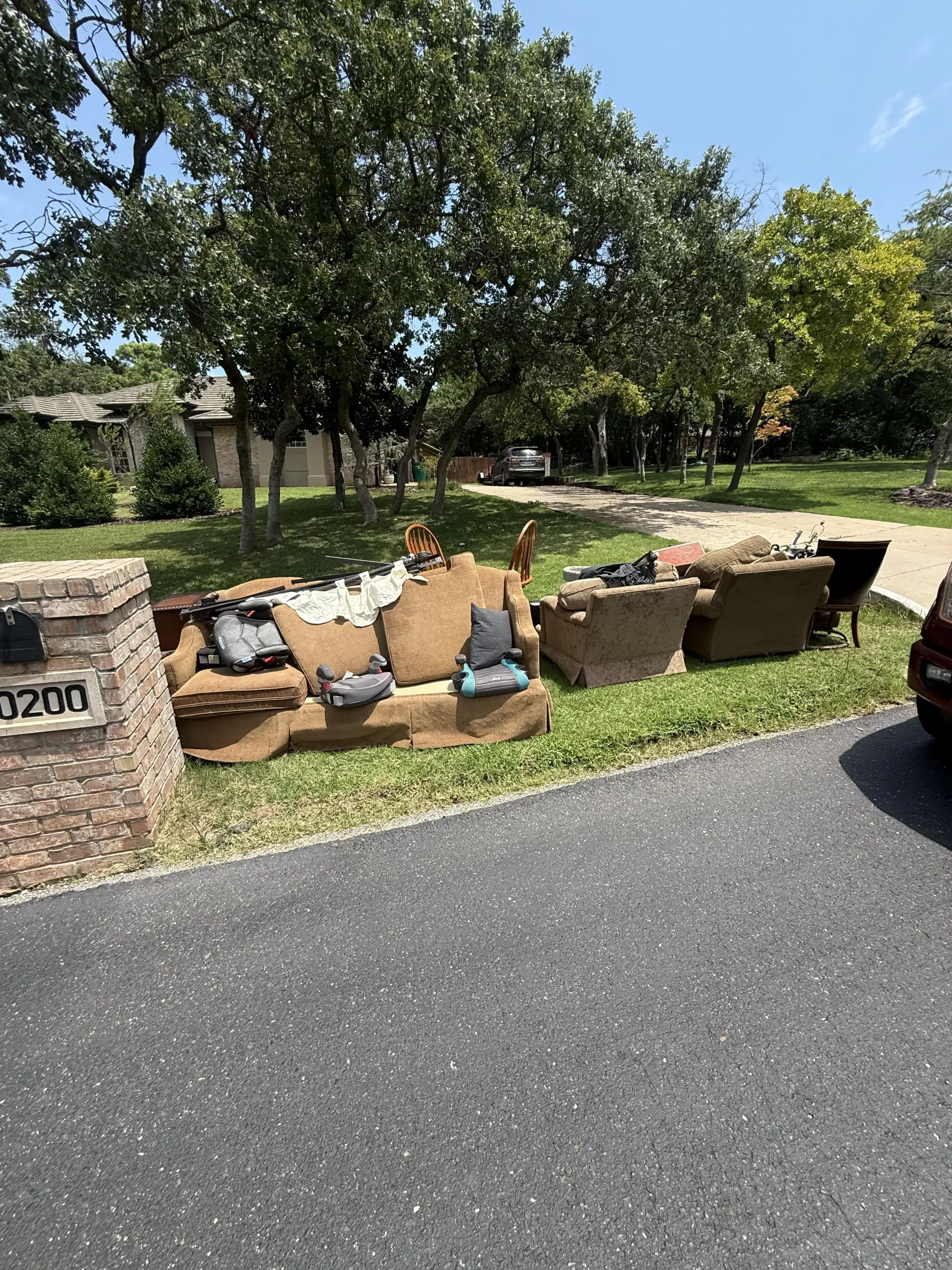 Suburban roadside flower bed with stone planters, green trees, and asphalt street in the foreground