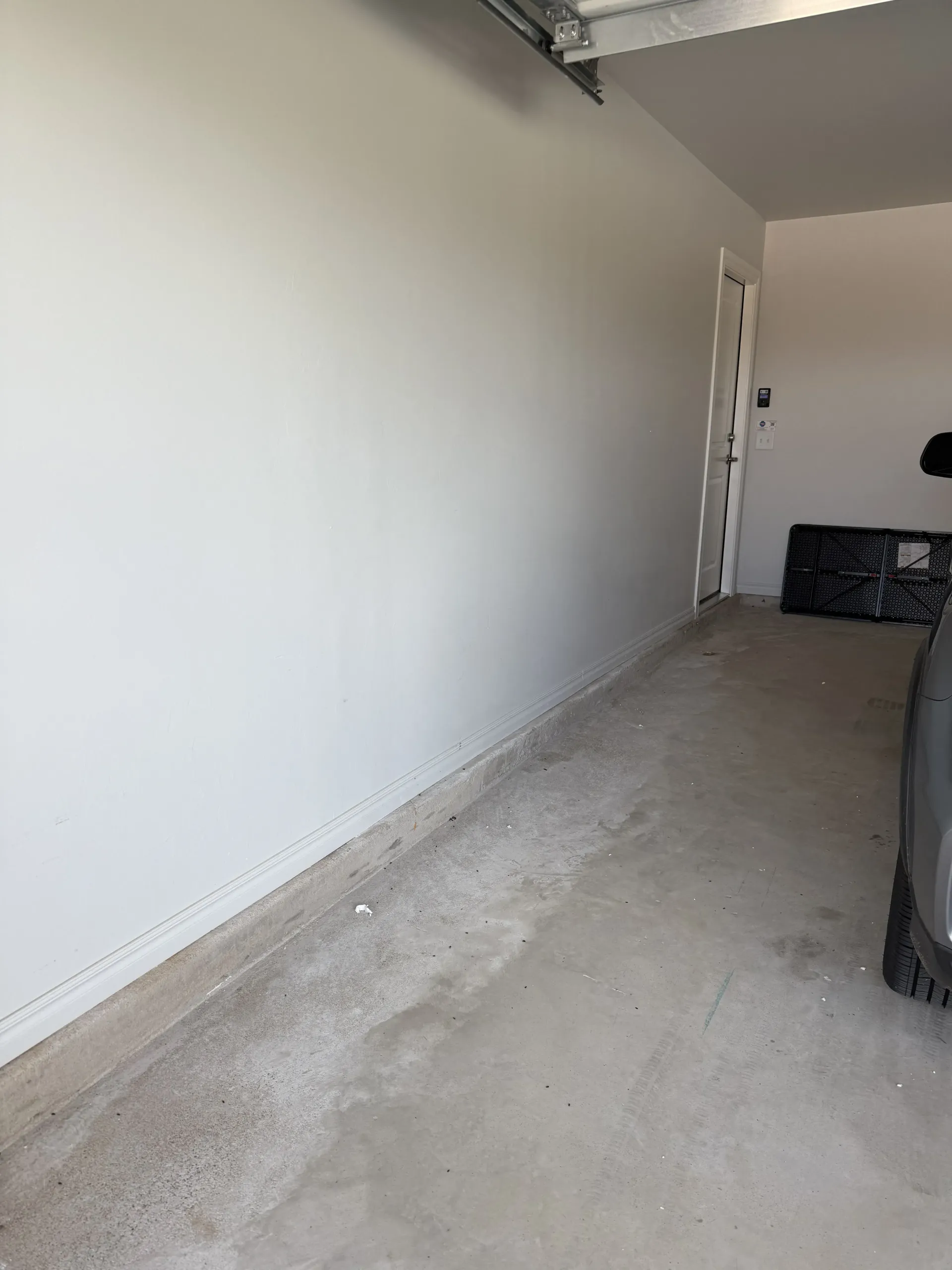 Empty garage with white walls, concrete floor, and a car parked along the right side.