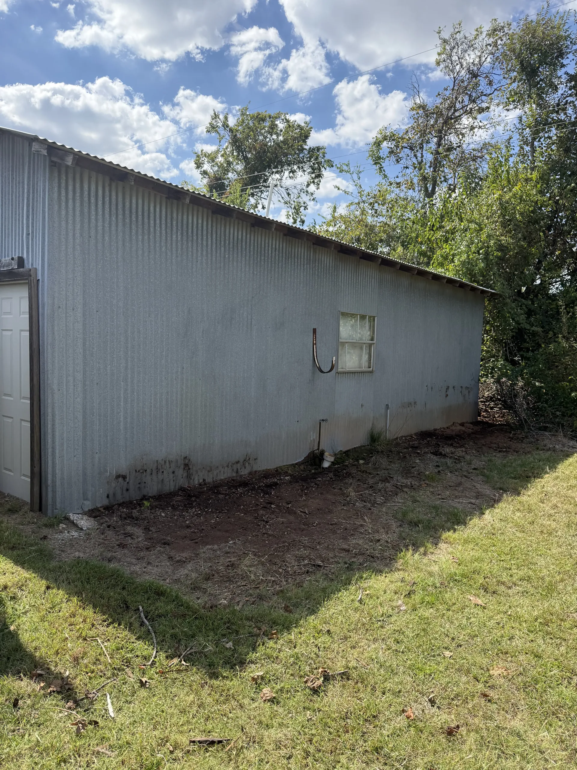 Gray corrugated metal building beside a grassy yard and trees under a partly cloudy sky