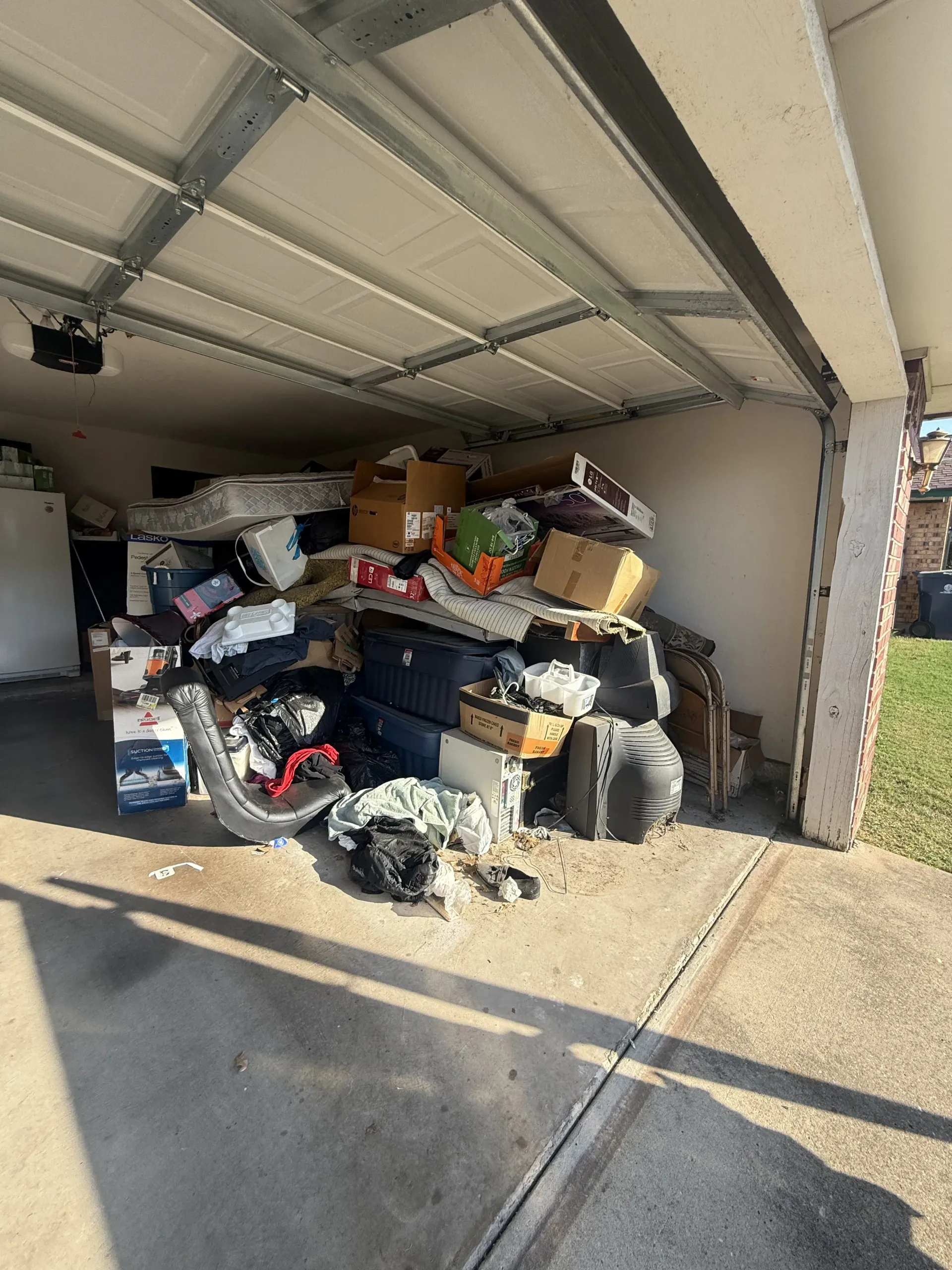 Garage packed with boxes, bags, and trash piled high under a partially open door.