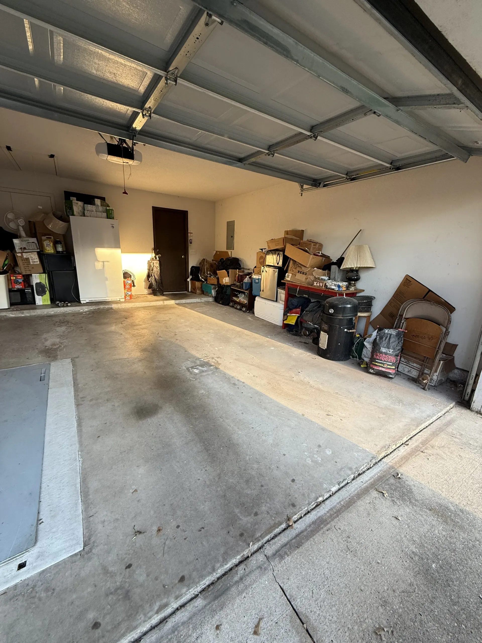 Garage interior with cluttered storage along the walls and a concrete floor under an open door.
