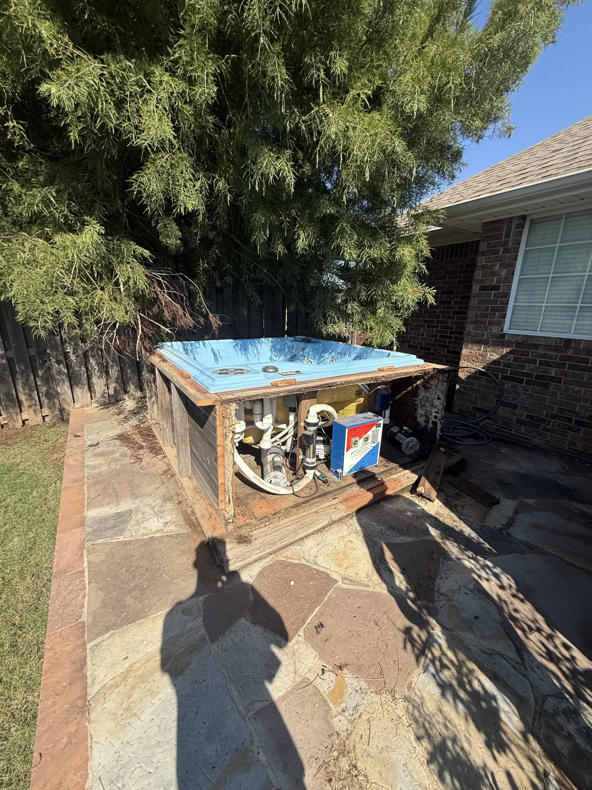 Old rusty utility unit with a blue top beside a house, under a tree in a sunny yard