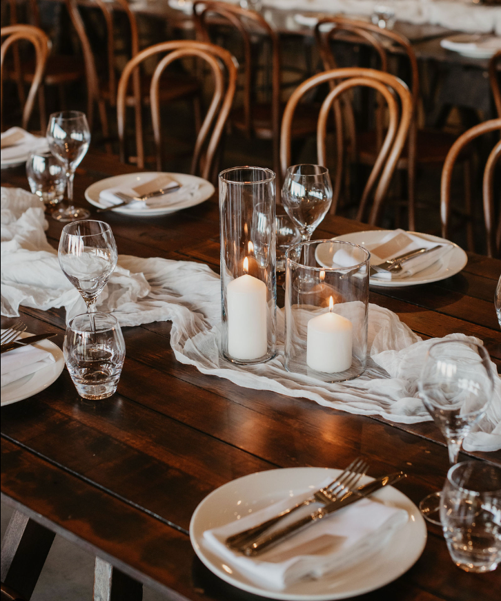 A table set for a wedding reception with plates , candles , glasses and silverware.