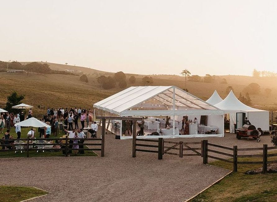 A group of people are gathered under a clear tent in a field.
