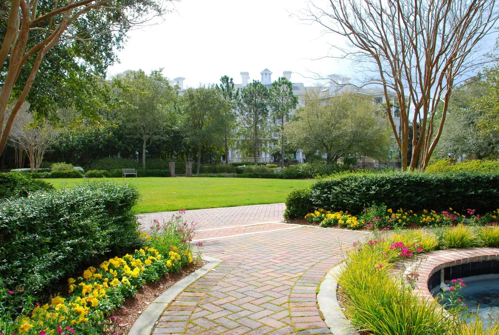 A brick walkway in a park with flowers and trees