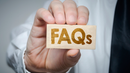 Hand holding a wooden block labeled “FAQs”