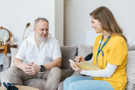 Two people sitting on a couch in a 상담 session, taking notes and talking in a bright living room