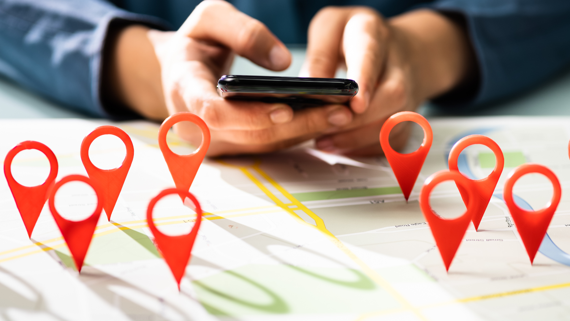 Hand holding a smartphone over a map with red location pins, suggesting navigation or location tracking