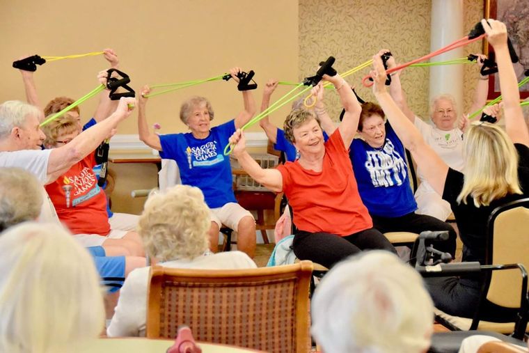 Group exercise class with seated adults raising colorful resistance bands in a bright room
