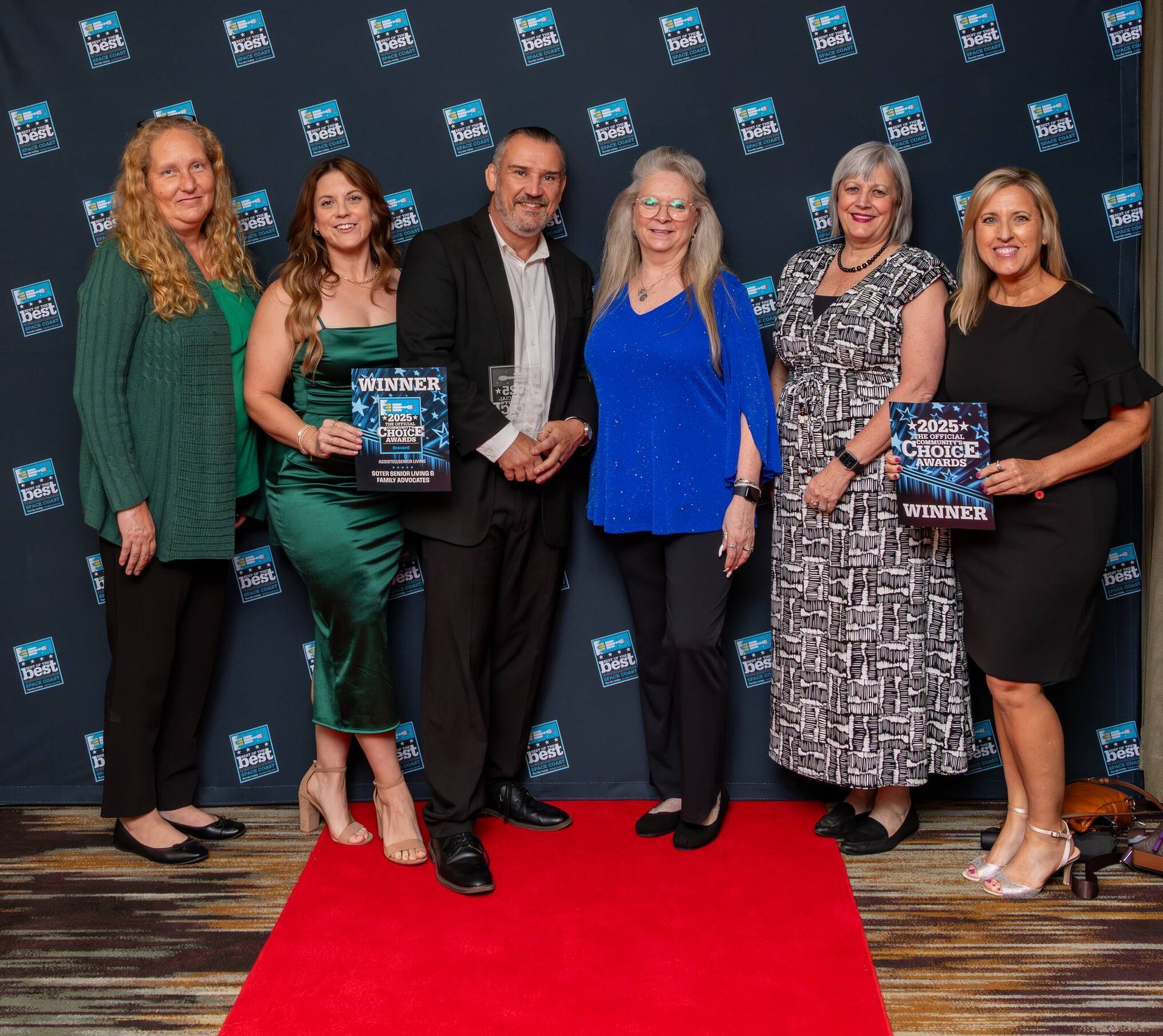 Six people pose on a red carpet holding awards at a formal event backdrop.