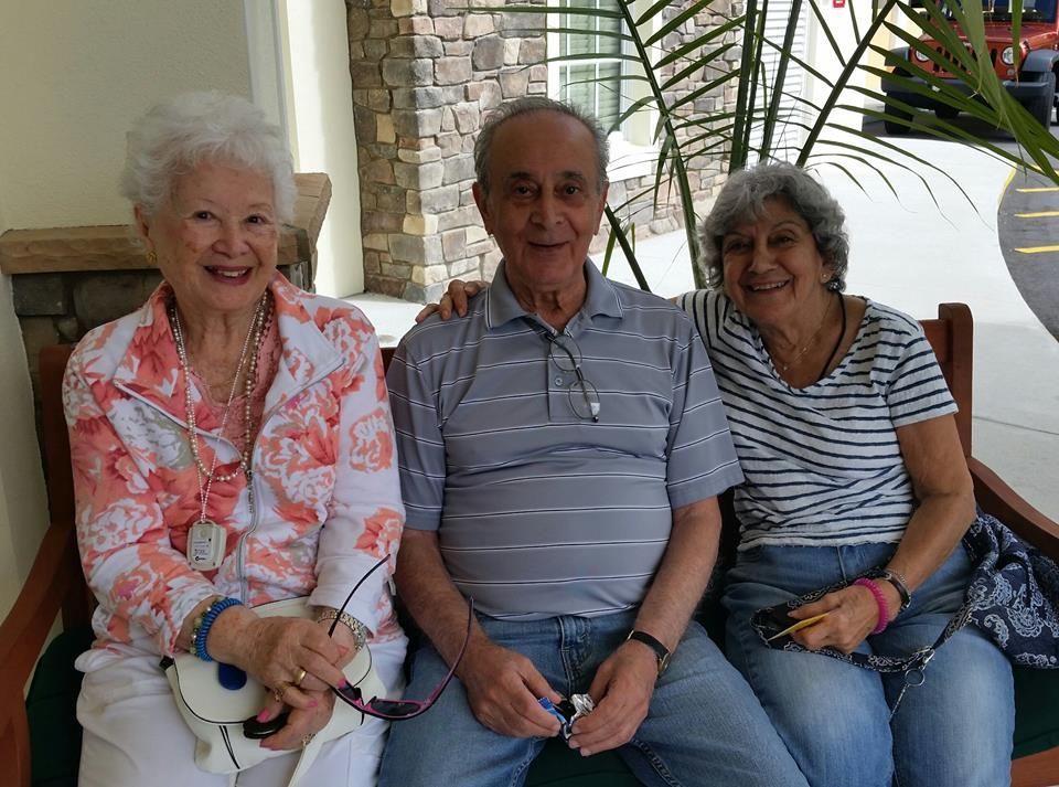 Three people sitting together on a couch, smiling indoors near a brick wall.