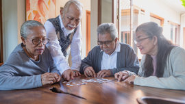 Four adults lean over a wooden table, examining papers together in a bright room.