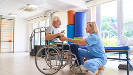 Physical therapist helping a wheelchair user exercise in a bright rehab room