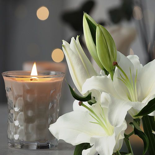 A candle is lit next to a white flower on a table.