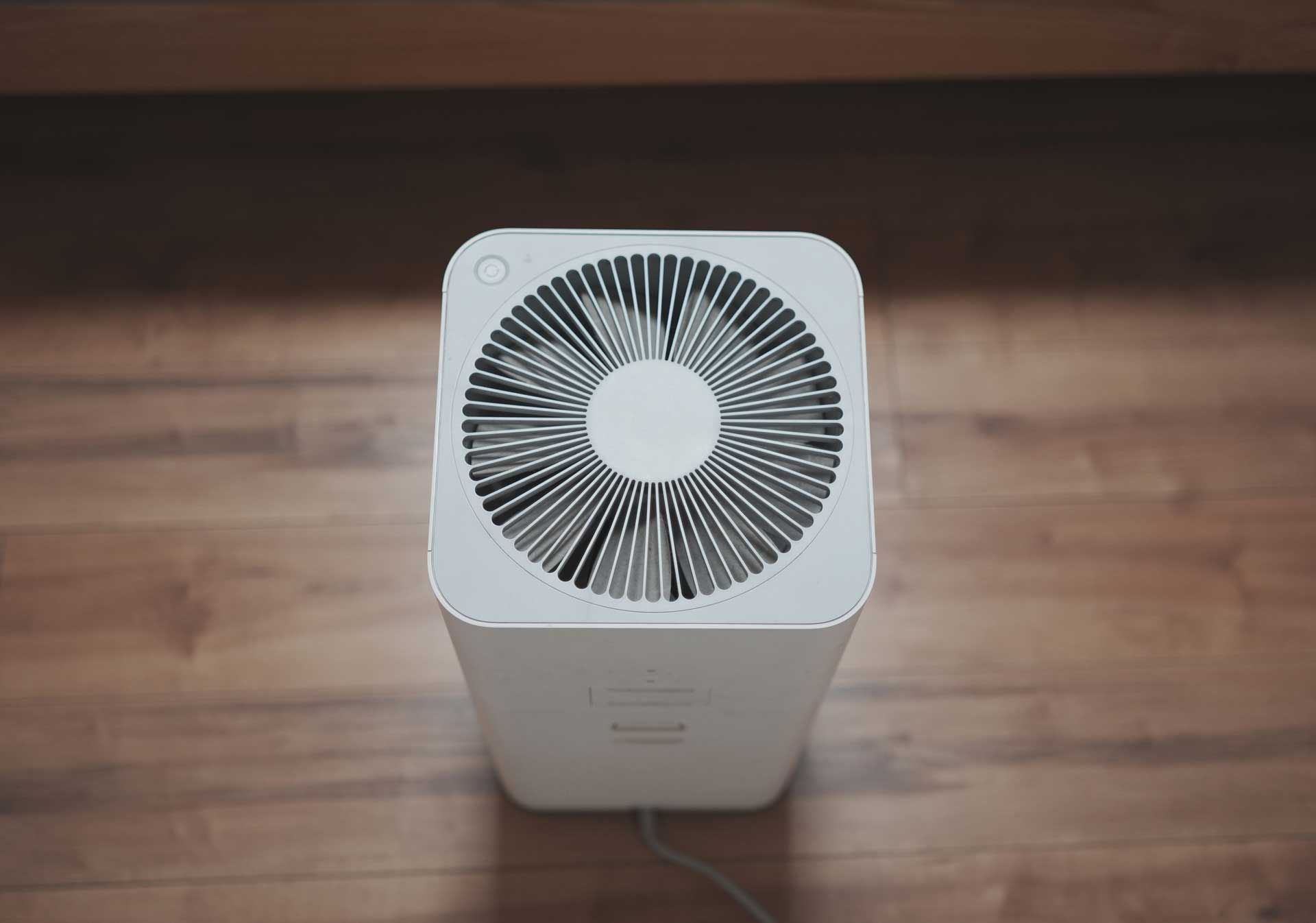 A white air purifier is sitting on a wooden floor.
