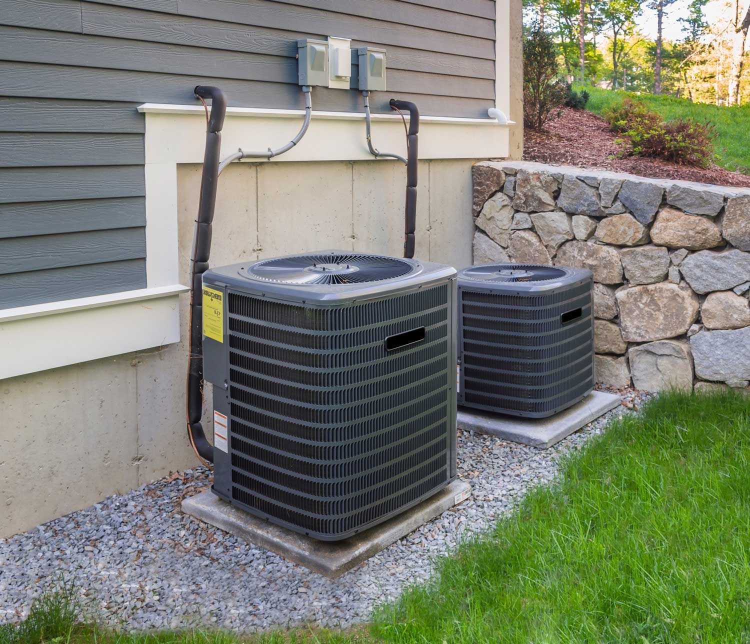 Two air conditioners are sitting on the side of a house.