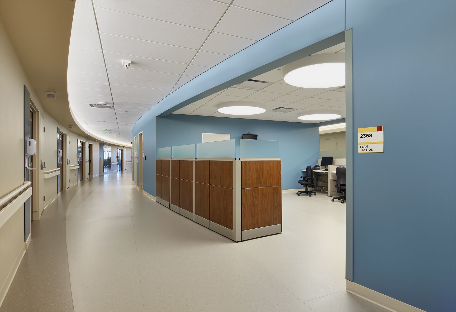 A hospital hallway with a cubicle in the middle of it.
