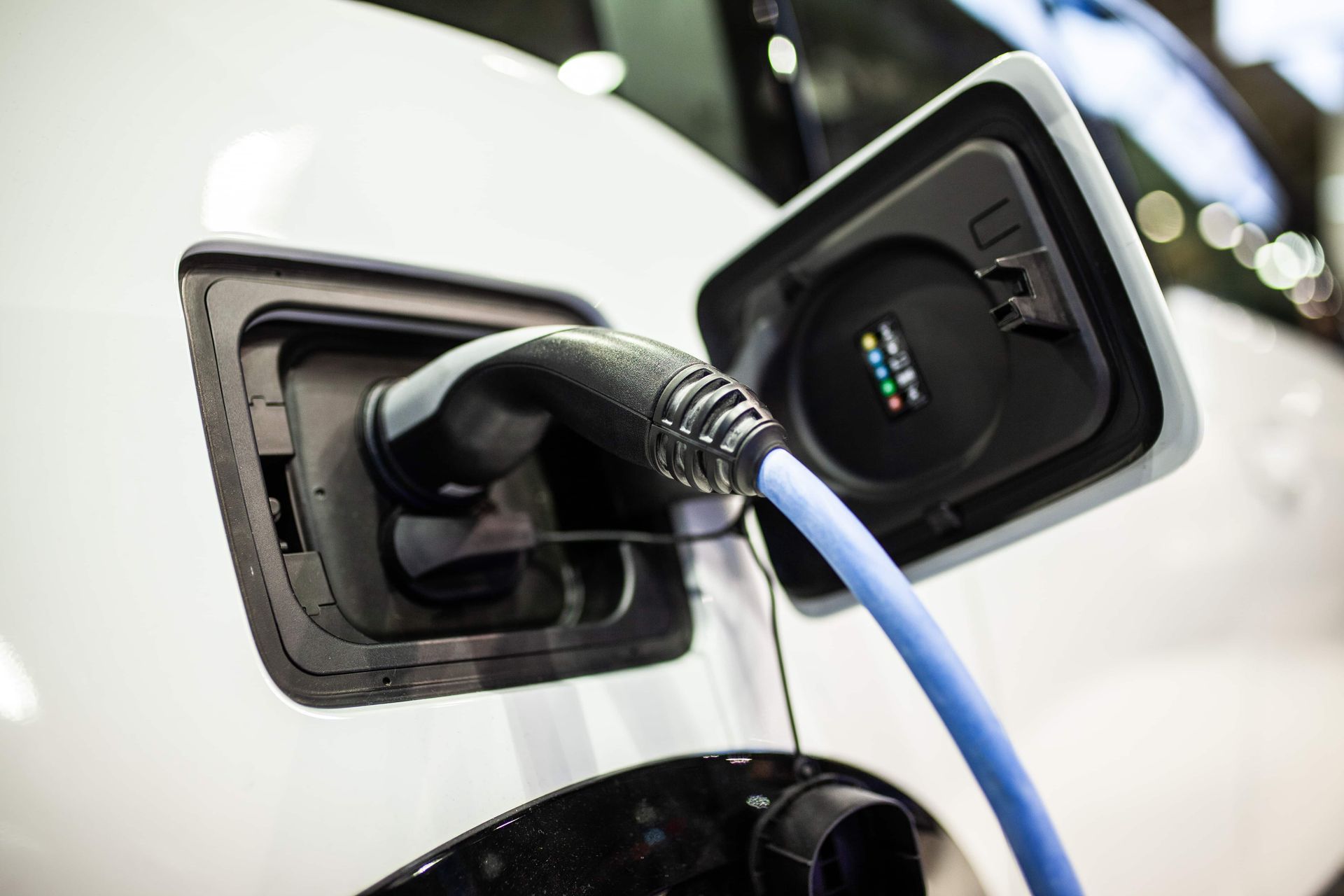 Electric car charging port with blue cable plugged into a white vehicle