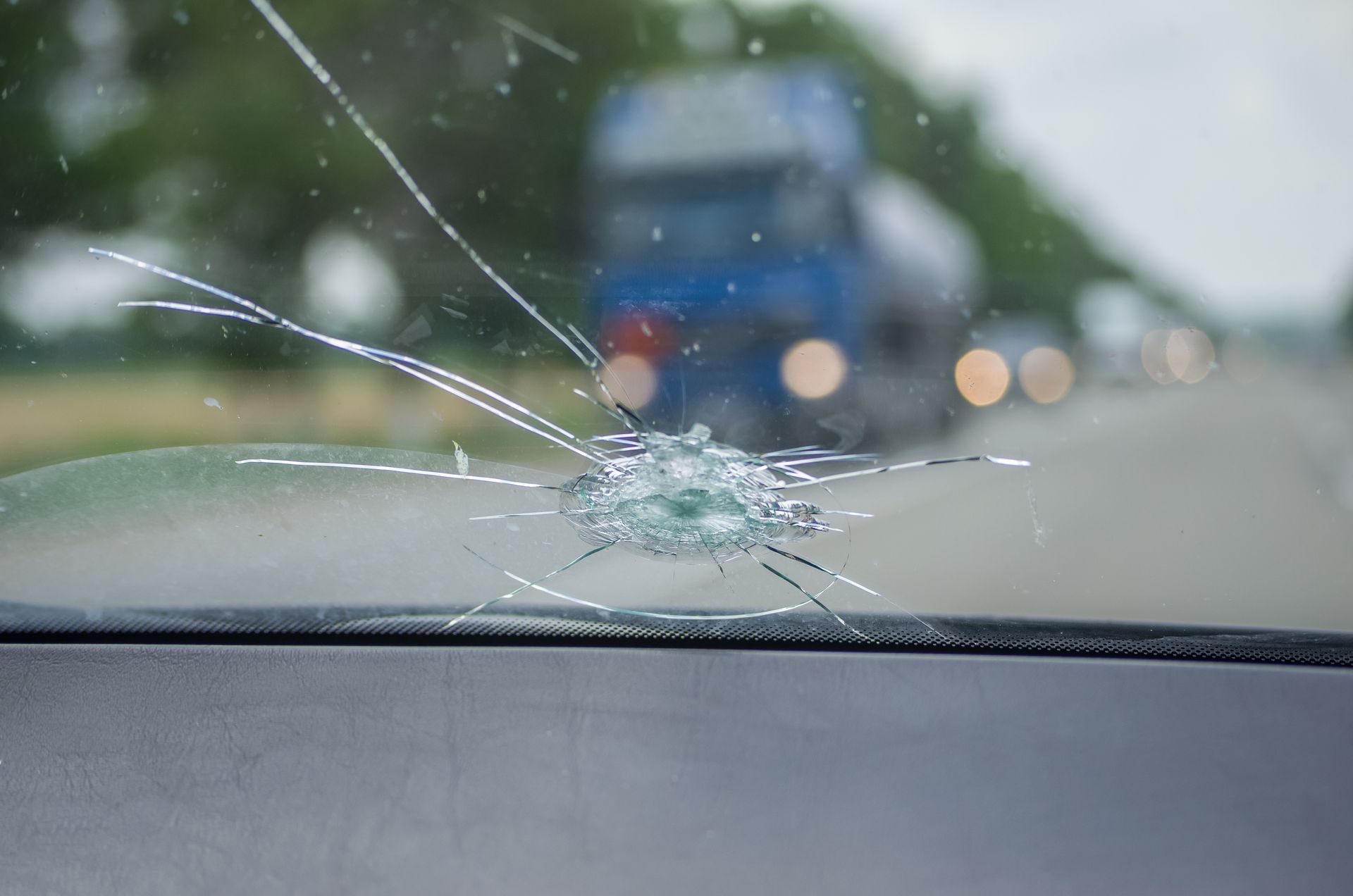 cracked windshield with a impact point and radiating fractures, viewed from inside a vehicle.