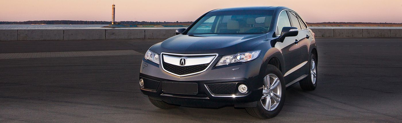 Dark gray sedan parked on a road at sunset with a city skyline in the background
