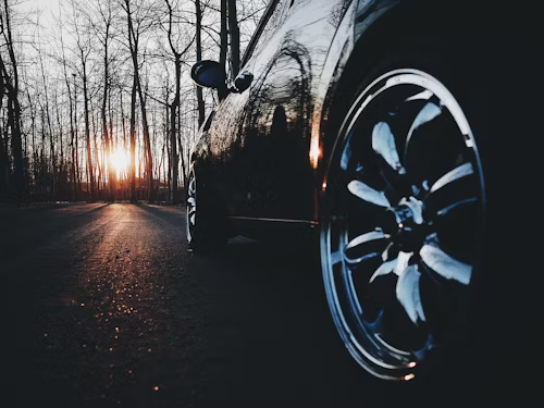 Black car parked on a road with trees; sunset in background. Shiny wheel, dark colors.
