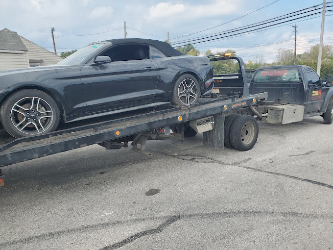 A black mustang is being towed by a tow truck.