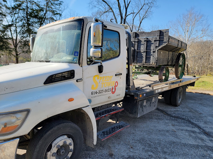 A white tow truck is carrying a wagon on the back of it.