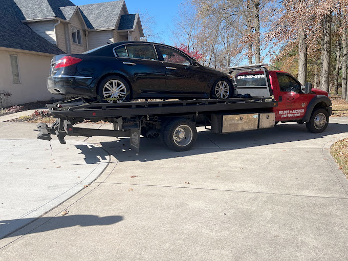 A tow truck is carrying a black car on the back of it.
