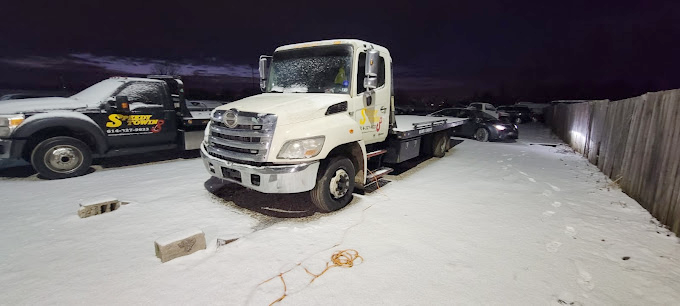 A tow truck is parked in the snow next to a fence.