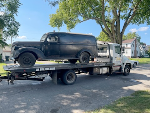 An old black van is being towed by a tow truck.