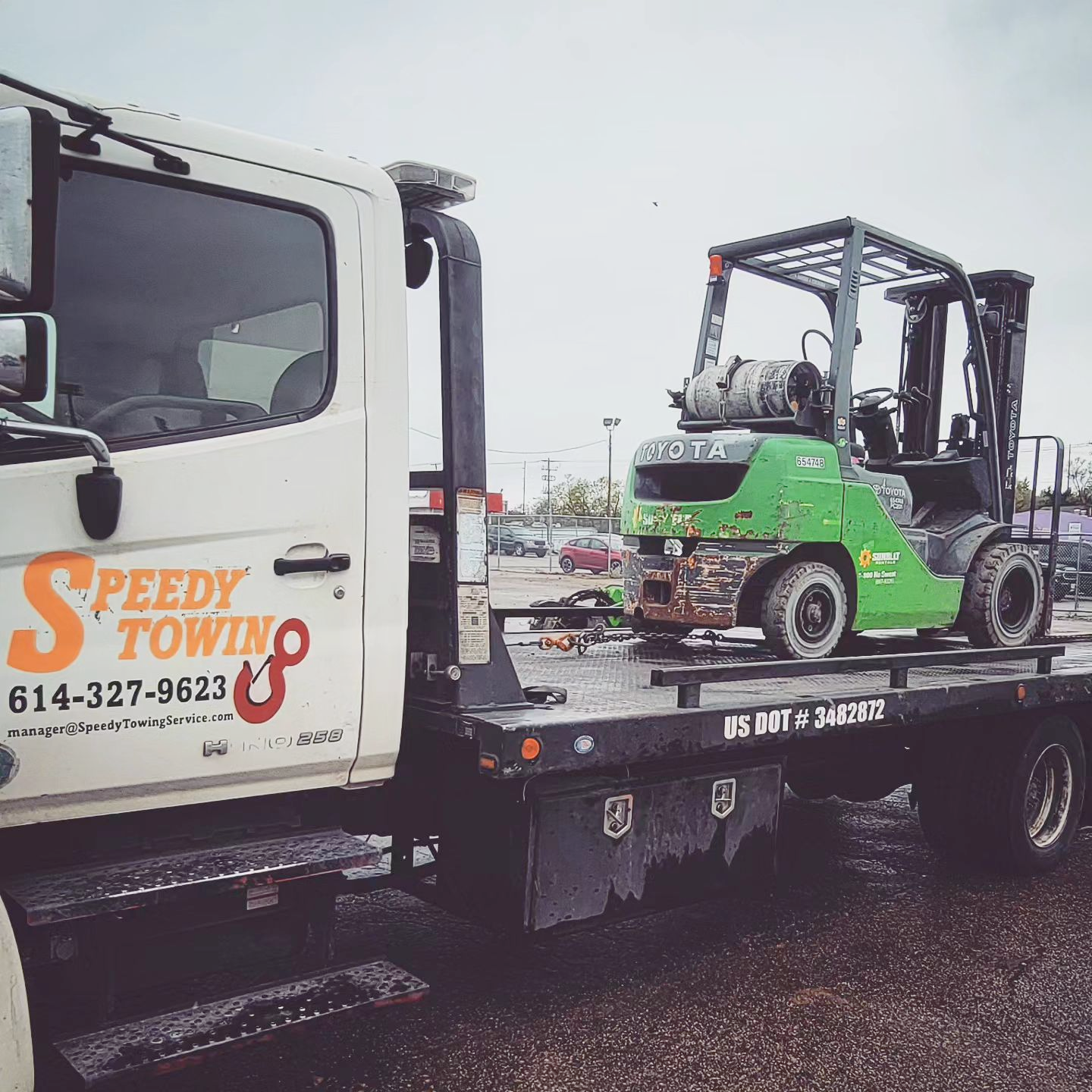 A green forklift is on the back of a speedy towing truck