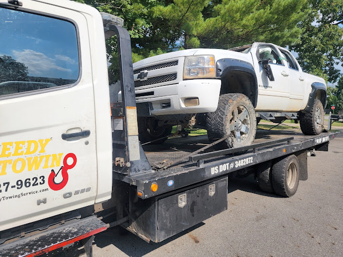 A white truck is sitting on the back of a tow truck.