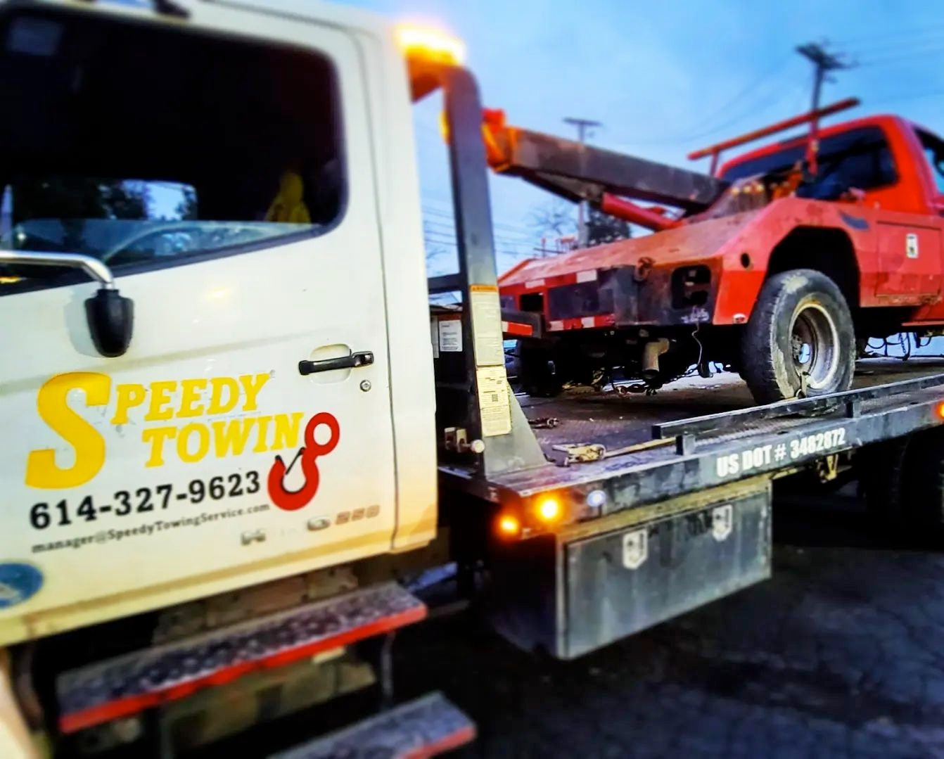 A speedy towing truck is carrying a red truck