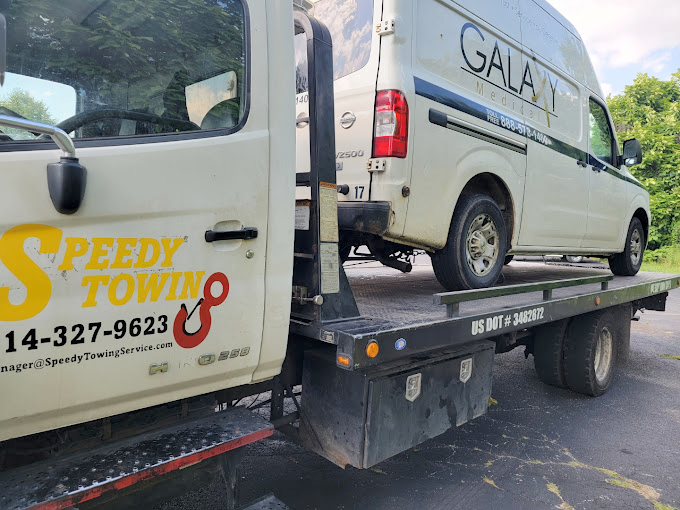 A white van is being towed by a speedy towing truck.
