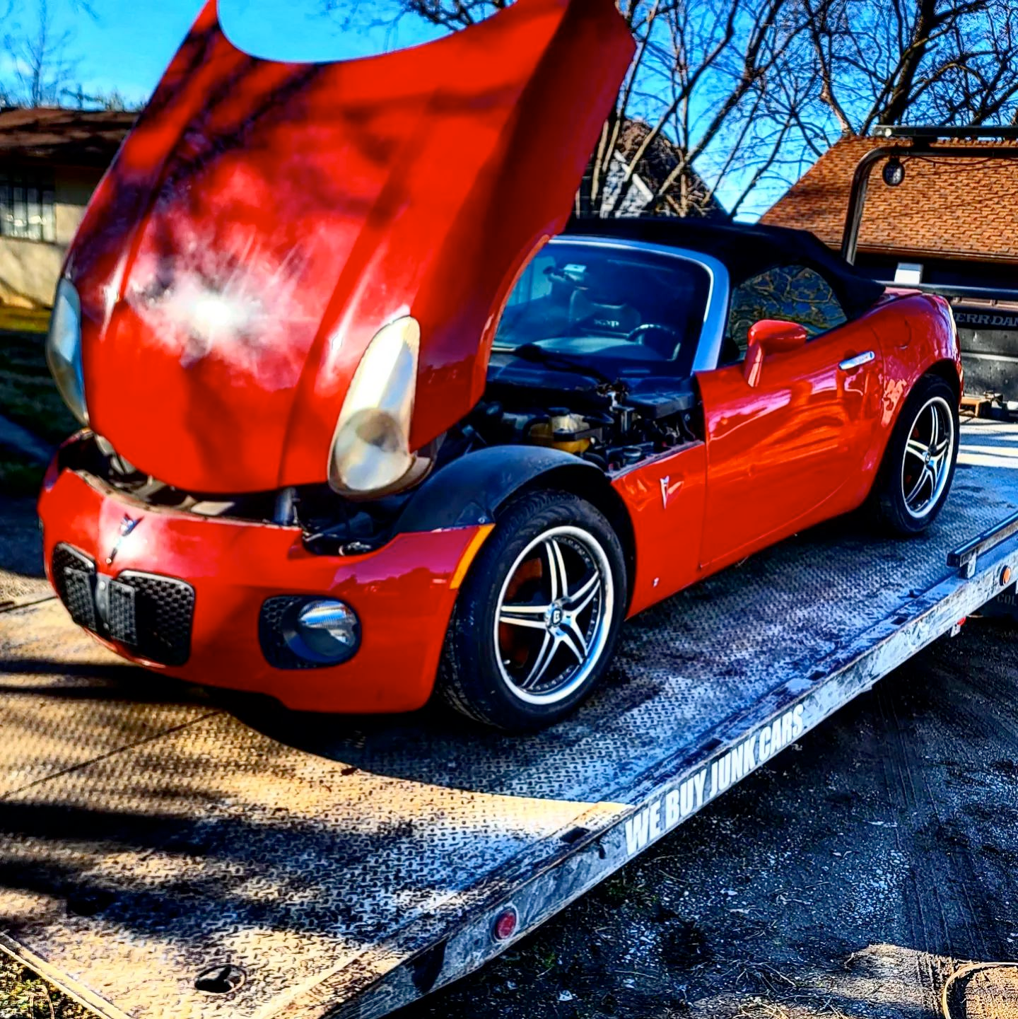 A red sports car with the hood up is on a tow truck