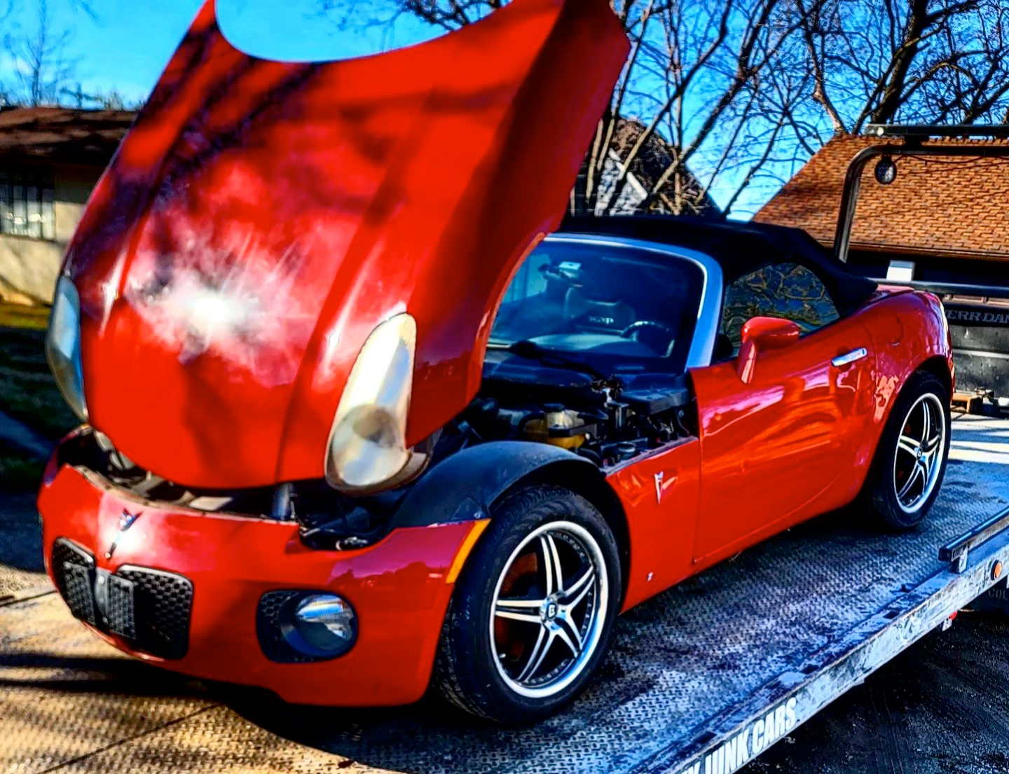 A red sports car with the hood up is on a tow truck