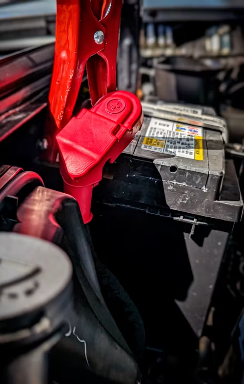 Red jumper clamp attached to a car battery in an engine bay.