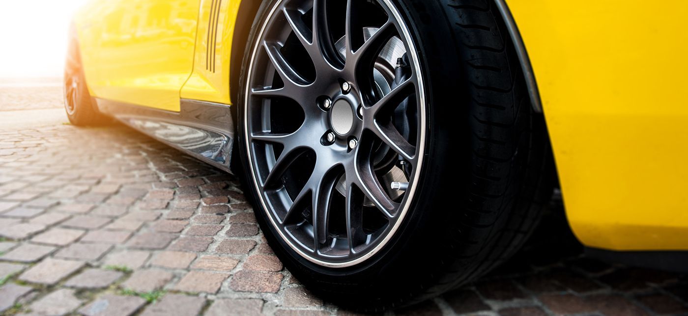 Close-up of a yellow sports car's tire and wheel on a cobblestone road.