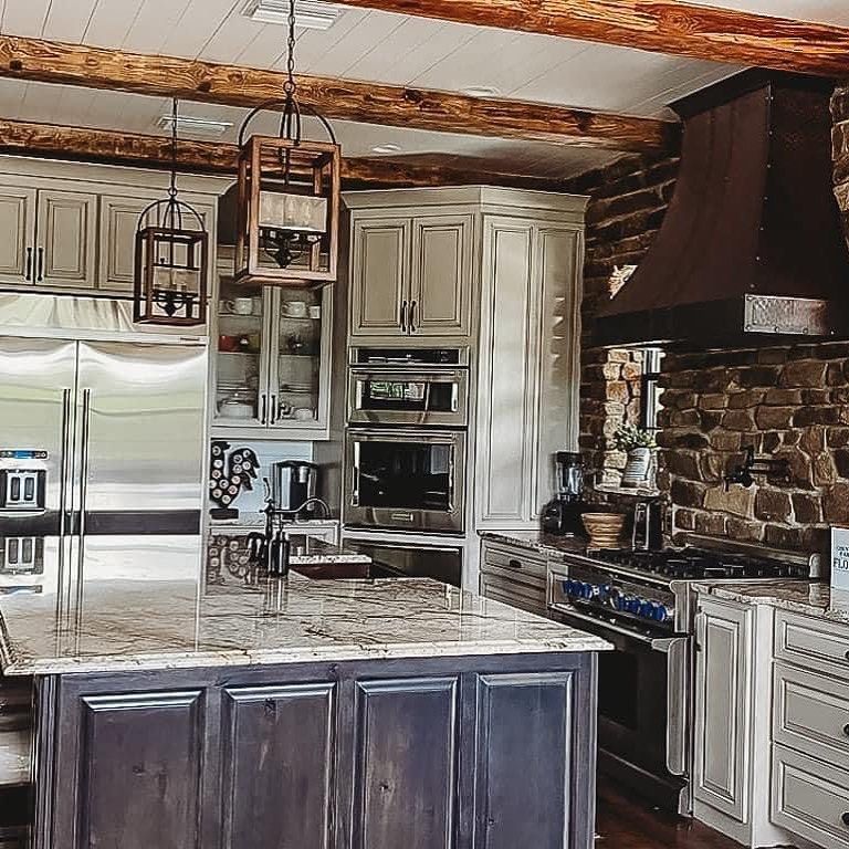Rustic kitchen with a stone wall, stainless steel appliances, and wood beams.