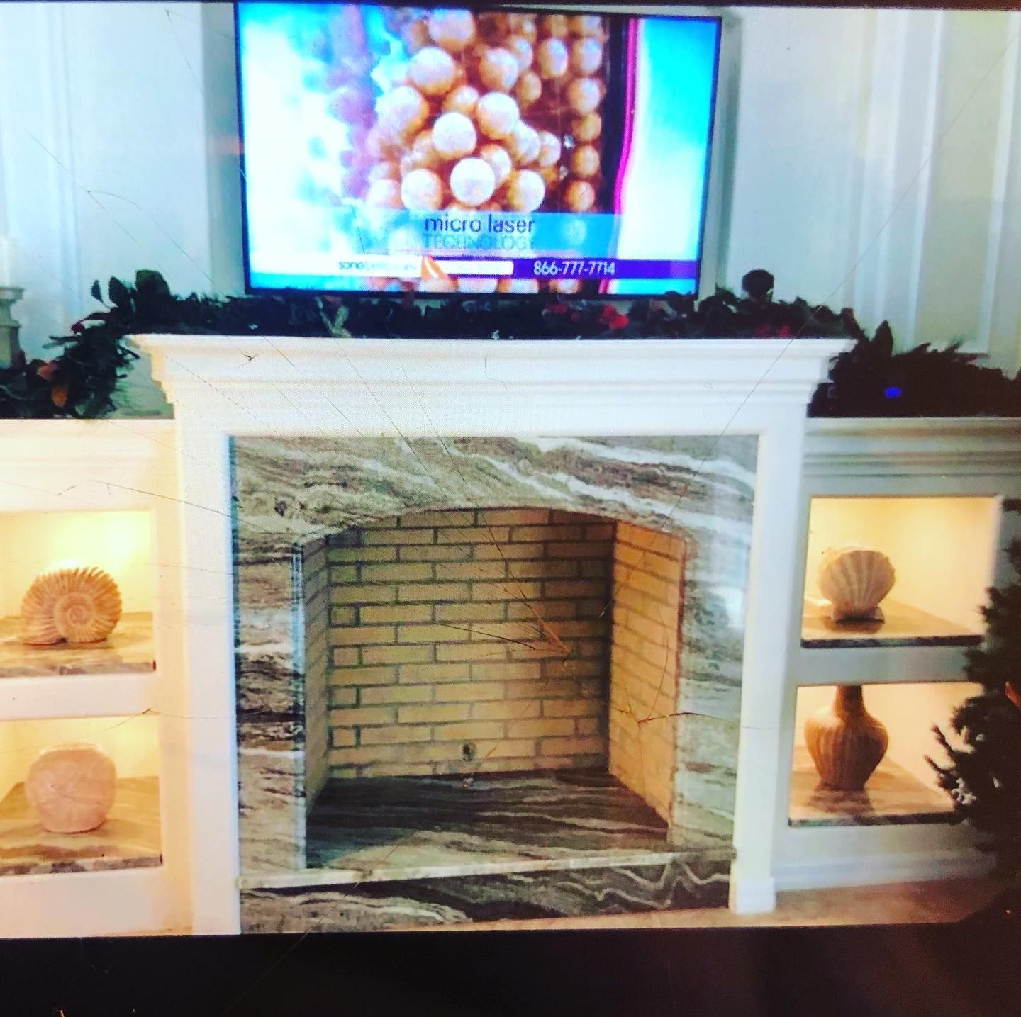 Fireplace with marble surround, brick interior, and built-in shelves displaying decorative objects. TV above.