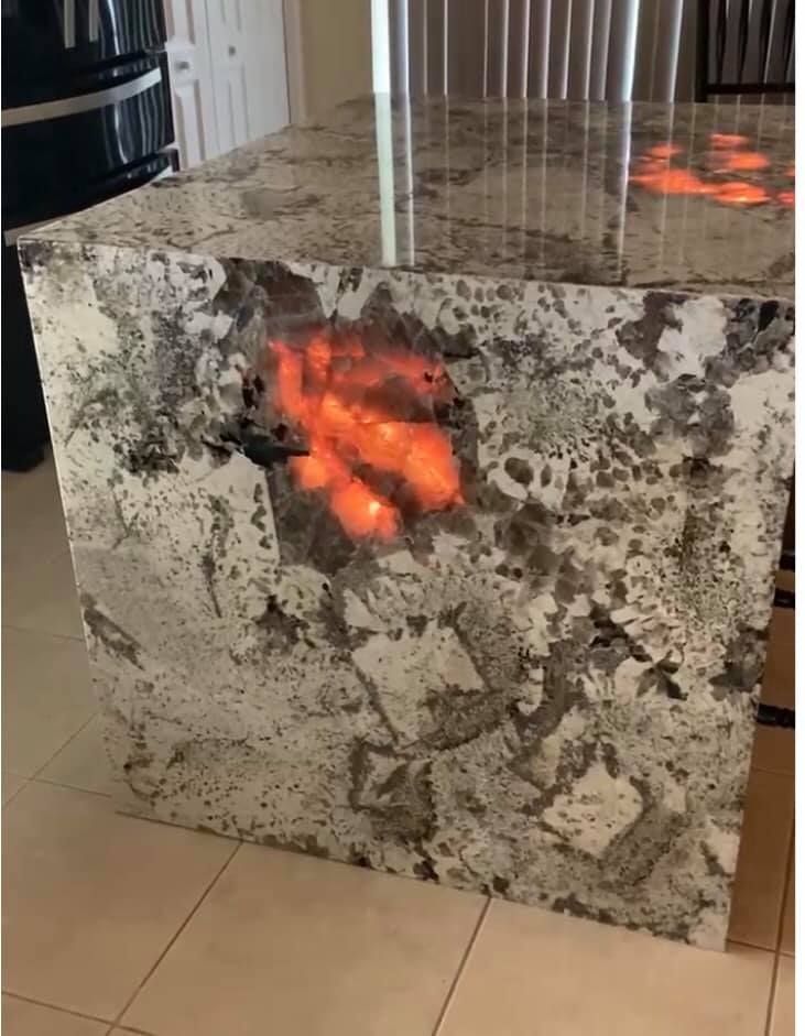 Granite kitchen island with an illuminated orange section, set in a light-tiled room.
